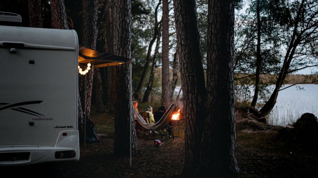 a couple sitting around a campfire outside of their camper which is situated on the shore of lake tahoe amongst the trees