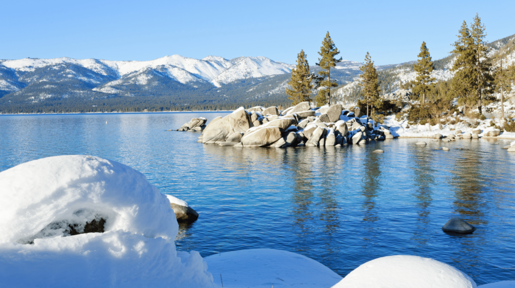 snowy rocks along lake tahoe with snow capped mountains in the background